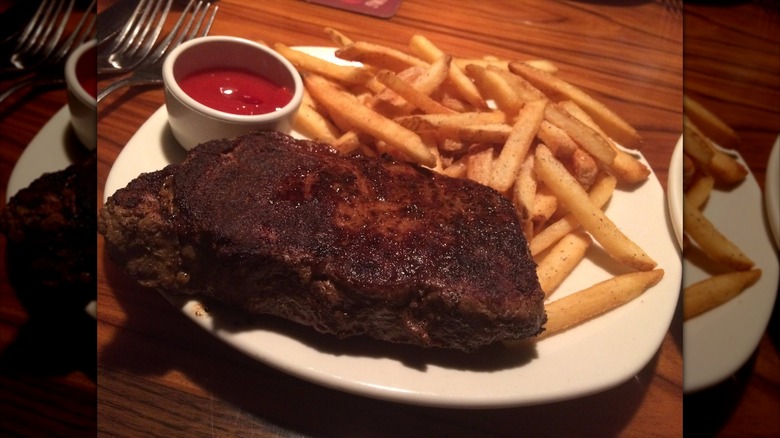 Well-done steak and fries on plate with side of ketchup