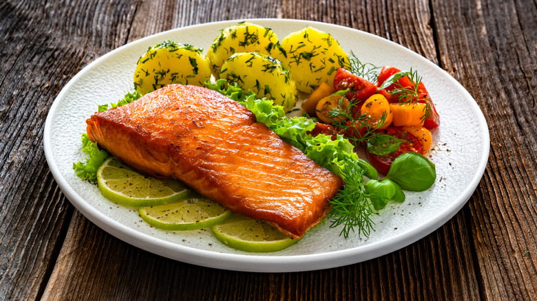 Salmon with veggies on white plate atop wooden table