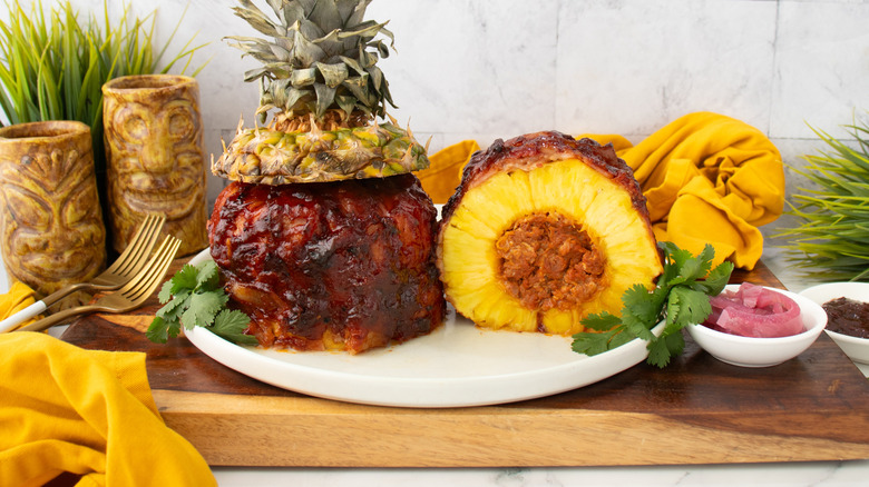 Pork-stuffed pineapple on plate with herbs
