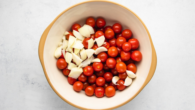 Cherry tomatoes, diced onion, and garlic cloves in mixing bowl