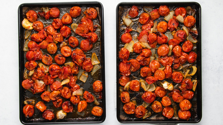 Roasted cherry tomatoes, onion, and garlic cloves on two baking sheets