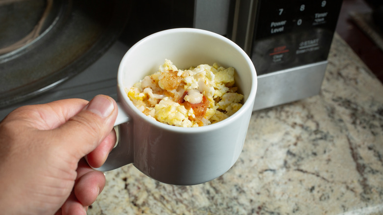 Person removing a cup of scrambled eggs from a microwave.