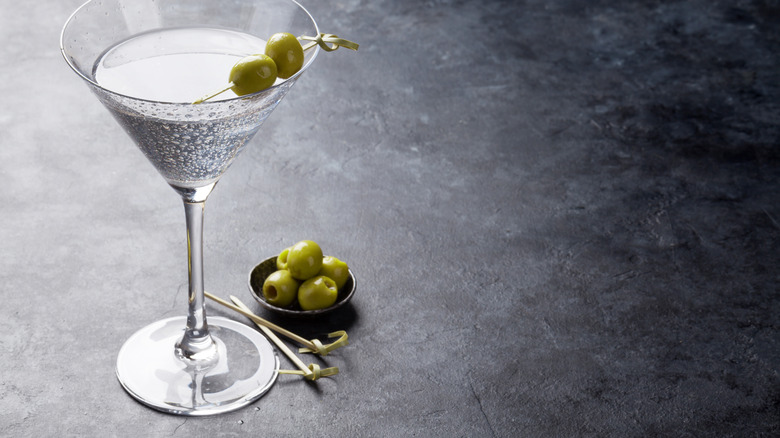 A dirty martini with olives in the glass and in a bowl