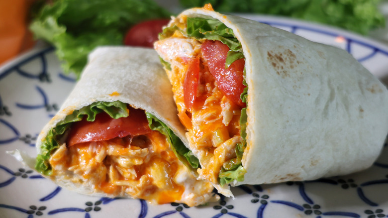 a sliced Buffalo chicken wrap with lettuce and tomatoes on a plate