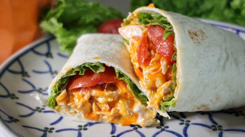 sliced, plated shredded Buffalo chicken wrap with lettuce and tomatoes