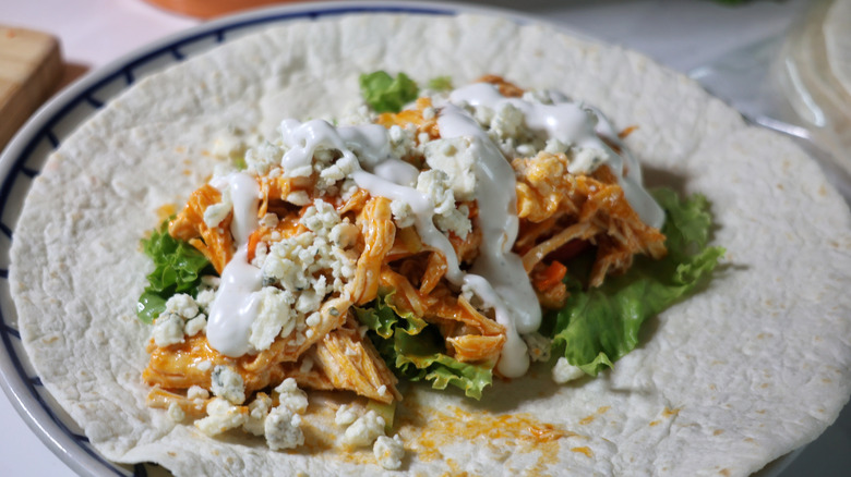 flour tortilla on plate topped with lettuce, shredded Buffalo chicken, blue cheese crumbles, and ranch dressing