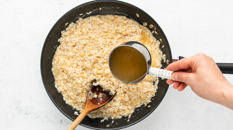 Pouring broth into pan of risotto