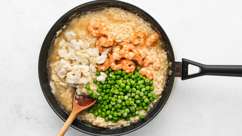 Adding shrimp, crab meat, and peas to pan of risotto