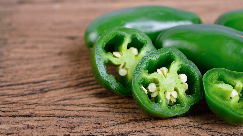 Whole and sliced jalapeños on wood surface