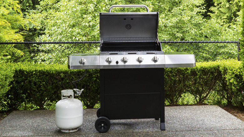 A propane tank next to a gas grill