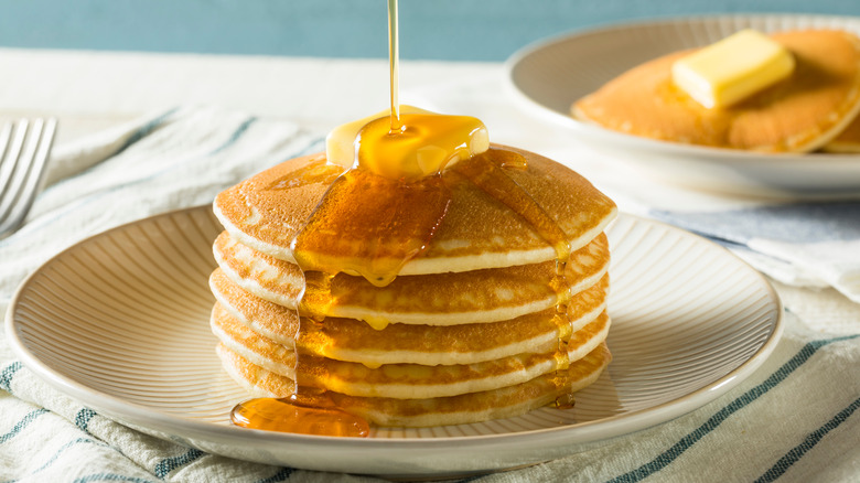 Syrup getting poured over a stack of pancakes