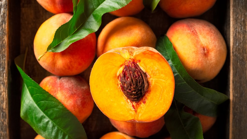 Ripe peaches in box with leaves, one cut in half