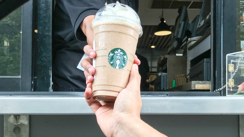 Employee handing Starbucks drink to customers at drive-thru