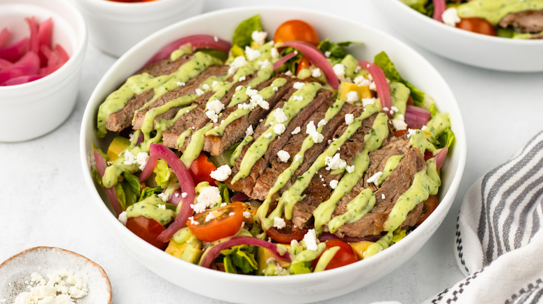 Bowl of steak taco salad with avocado dressing and crumbled cotija cheese