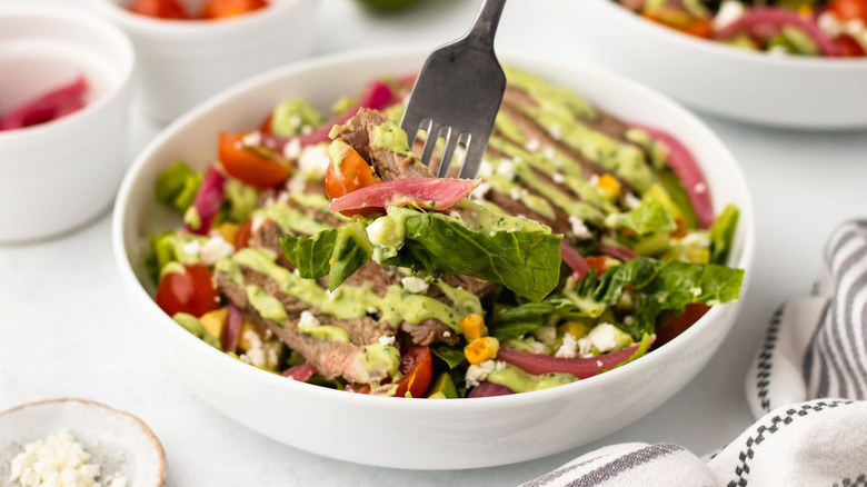 Forkful of steak taco salad hovering above the rest of the salad in bowl