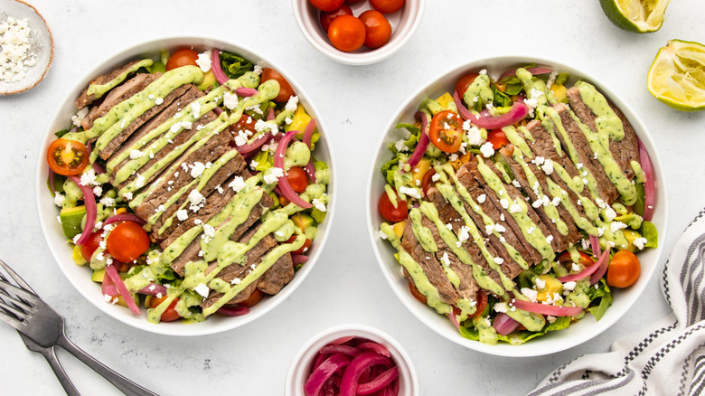 Two bowls of steak taco salad with avocado dressing and crumbled cotija cheese