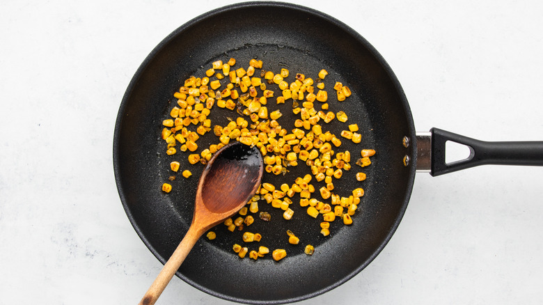 Charred corn in frying pan with wooden spoon