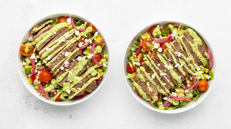 Two bowls of steak taco salad with avocado dressing and crumbled cotija cheese