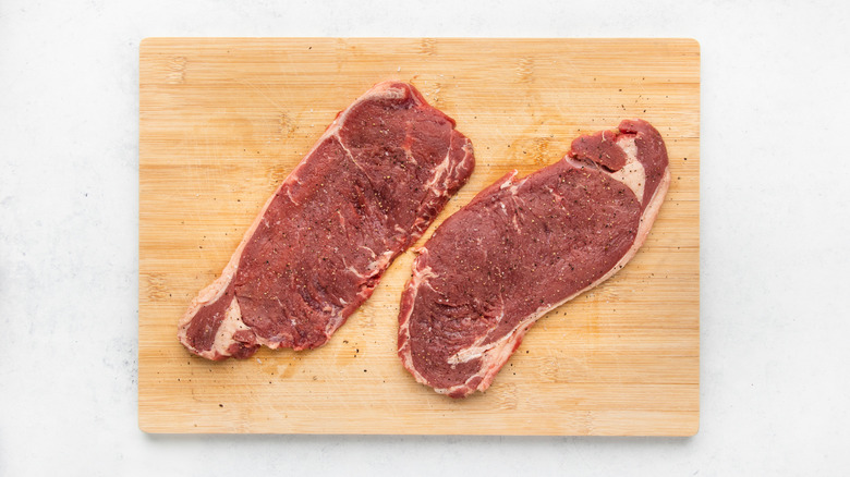 Two seasoned sirloin steaks on wooden cutting board
