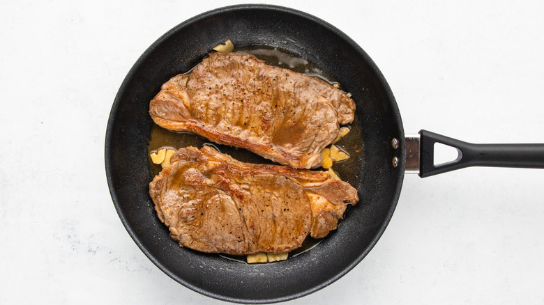Two steaks in frying pan with melted butter and sliced garlic