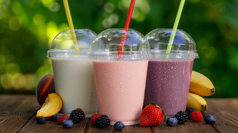 Three iced drinks in plastic cups on wood table outside