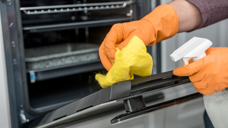 Hands in orange gloves spraying oven with cleaning liquid