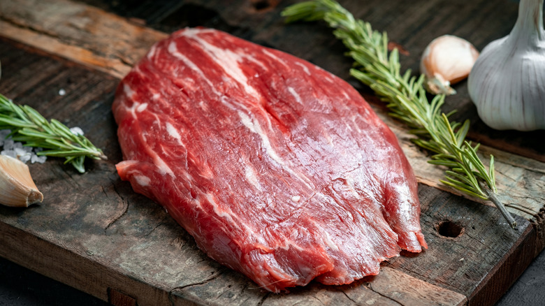 Raw flank steak on cutting board with rosemary