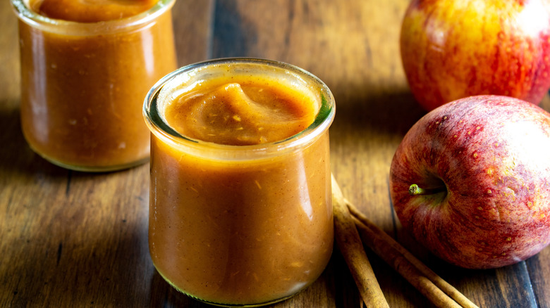 A jar of apple butter with apples nearby