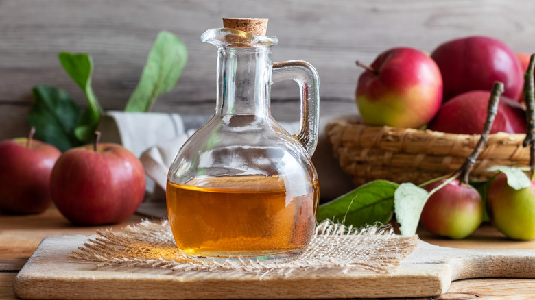 Clear jar of apple cider vinegar next to apples