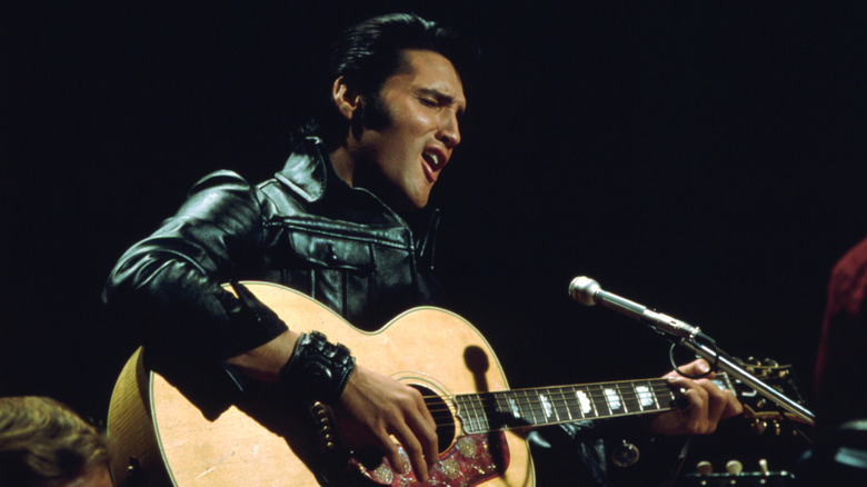 elvis presely in black leather suit, playing acoustic guitar