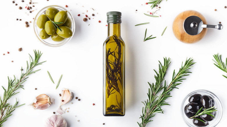 Bottle of olive oil and bowl of olives on white surface