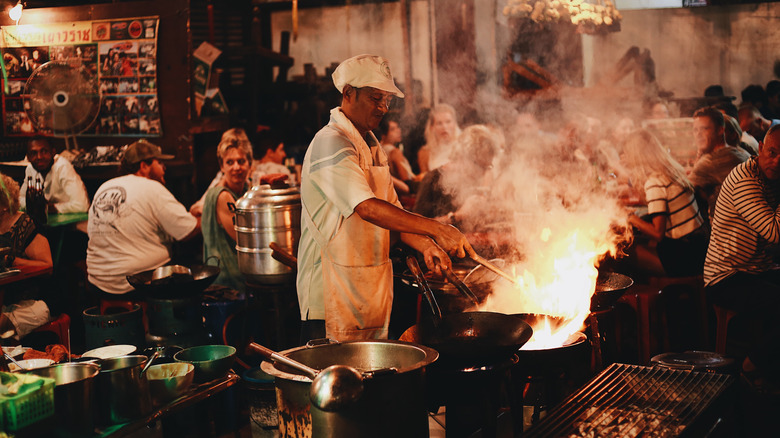 Street food vendor cooking with diners in background
