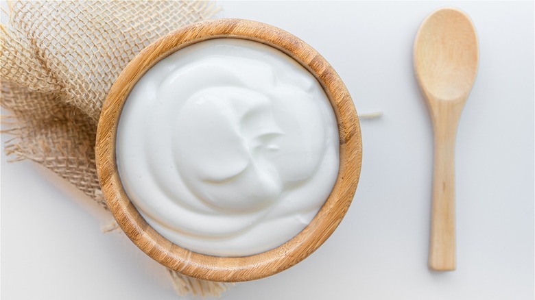 Wood bowl with white yogurt next to wood spoon