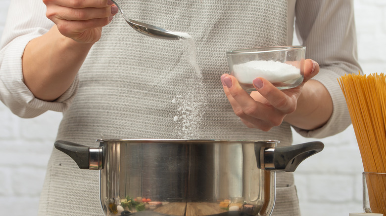 Person sprinkling salt into pasta pot