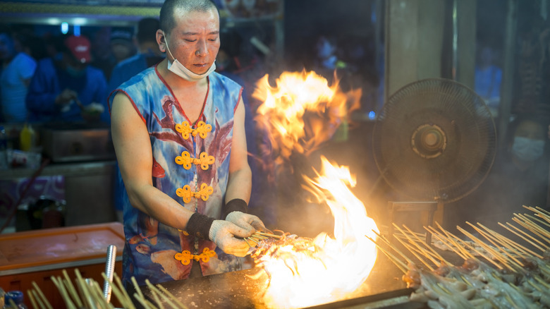 Street vendor cooks squid skewers over open flame