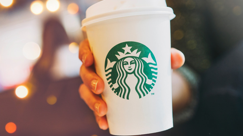 A hand holding out a Starbucks cup