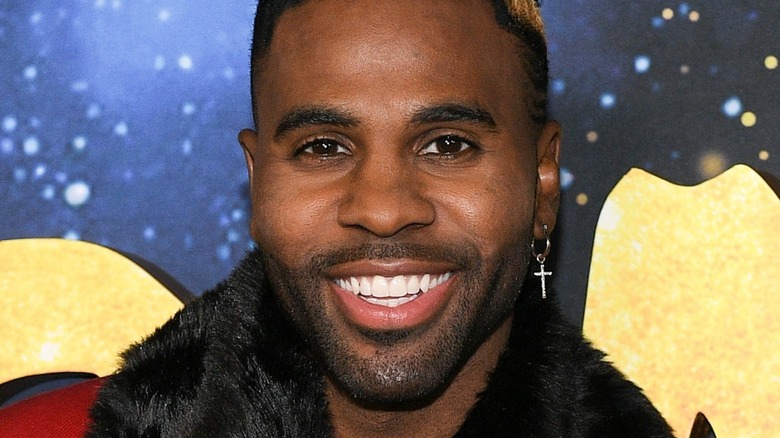 Jason Derulo smiles with cross earring and fur jacket