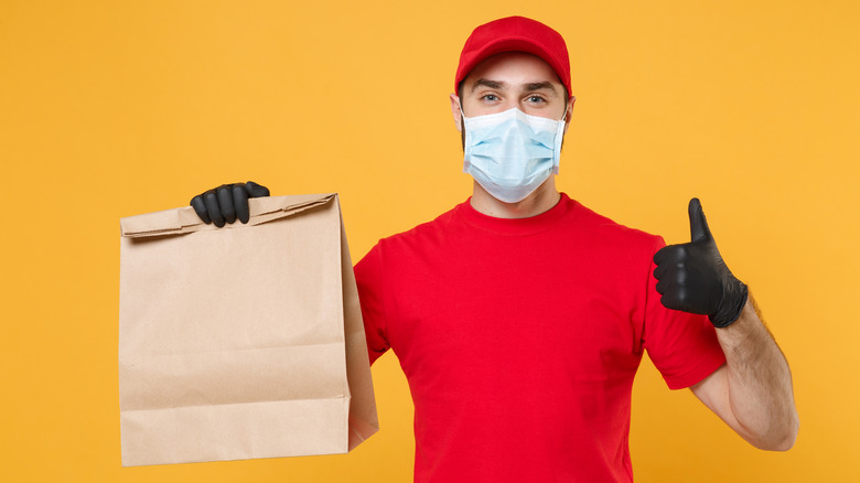 man with mask and gloves holding bag of food