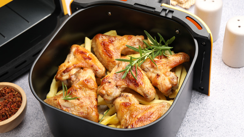 Chicken wings with french fries and herbs inside air fryer basket.