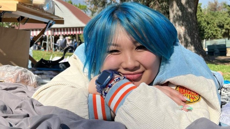 Soy Nguyen with blue hair laying on grass