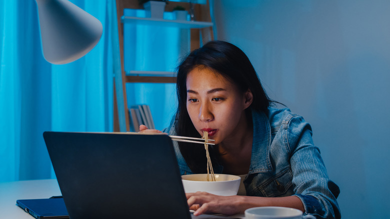 student eating noodles in front of computer
