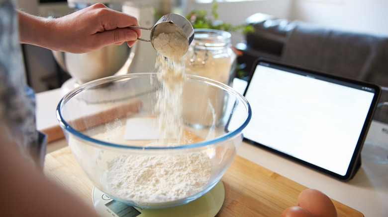 Hand measuring flour into mixing bowl on scale at kitchen counter