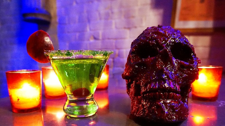 Green martini next to juicy skull and candles