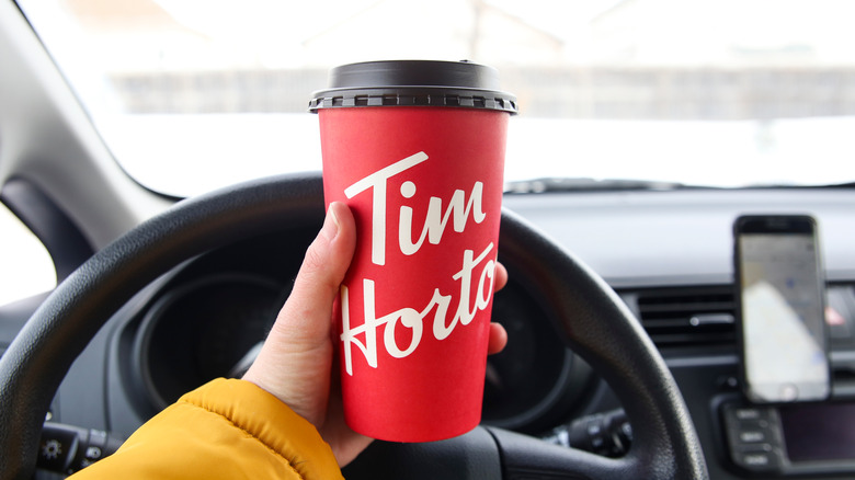 A person in their car holding a cup of Tim Hortons coffee