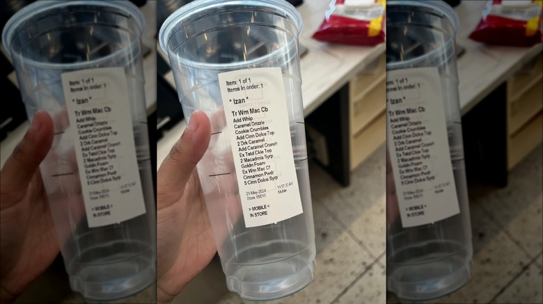 Starbucks barista holding plastic cup with lengthy drink instructions on the side