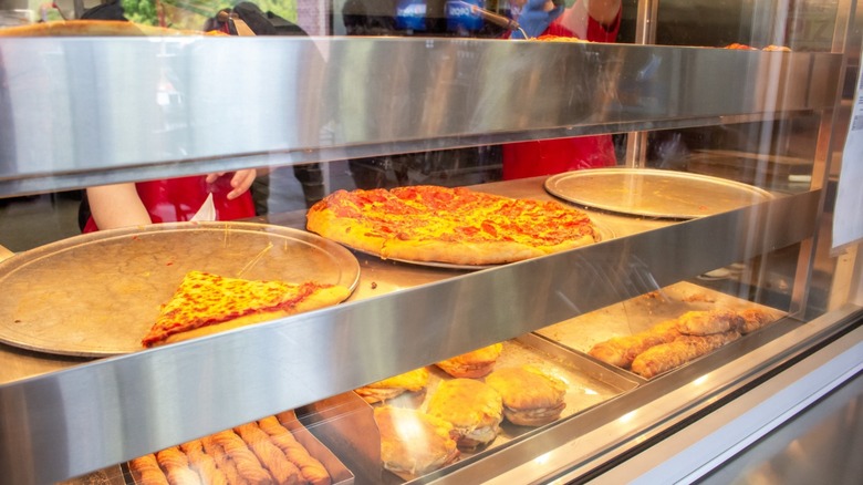 Costco pizzas and other foods under warming lamps inside the food court.