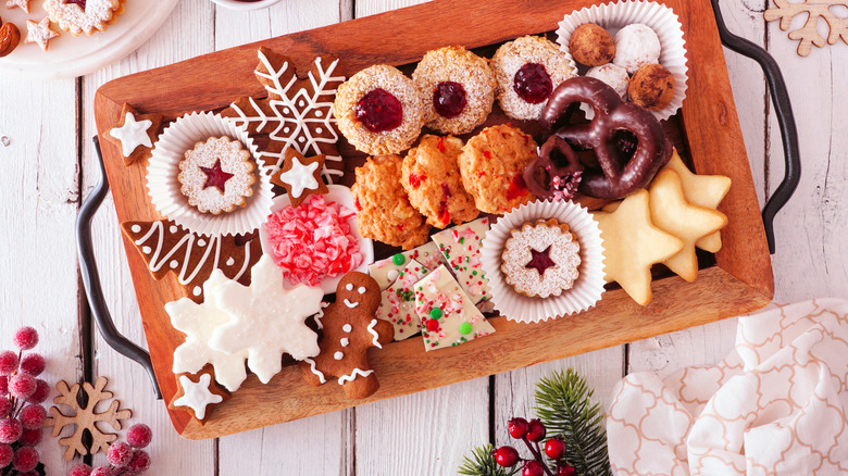 metal handled wooden tray of assorted Christmas cookies and candy on white wooden table