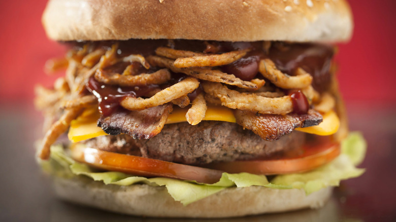 Close-up of burger with onion rings and barbecue sauce.