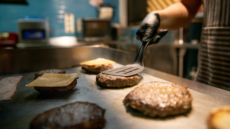 Chef cooking cheeseburgers on restaurant griddle.