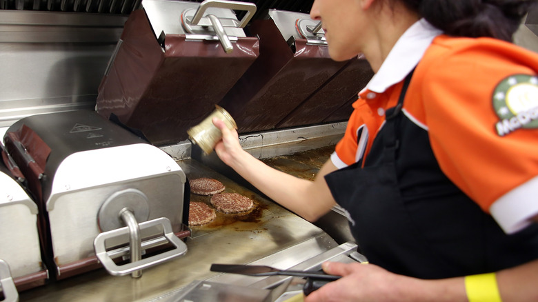 McDonald's employee seasoning burger patties as they cook on the grill.